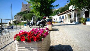 A cobblestone street with a flower planter in the foreground, a scooter parked on the side, and a building with a tower in the background. - Casa Vacanza Circe (Sperlonga)