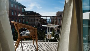 A balcony with wicker furniture, a small table, and a view of buildings and a clear sky. - Casa Vacanza Circe (Sperlonga)