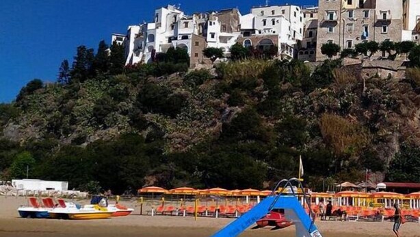 A boat docked near a beach with a building in the background. - Casa Vacanza Circe (Sperlonga)