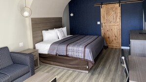 A bedroom with a bed, a bedside table, a chair, a wardrobe, and a hanging light fixture. - Palace Inn (Humble)