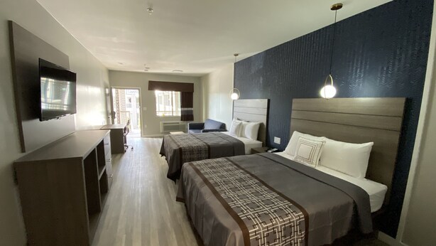 A hotel room with two beds, a TV, a desk, and a window. - Palace Inn (Humble)