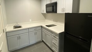 A modern kitchen with white cabinets, a black refrigerator, a microwave, and a sink. - Palace Inn (Humble)