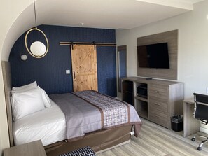 Habitació d'hotel moderna amb llit, escriptori, televisió i armari.
