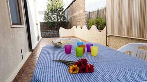 Una mesa al aire libre con mantel a cuadros, una cesta, tazas de colores y una silla.