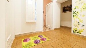 Un pasillo con suelo de baldosas, un felpudo con diseño floral, una puerta entreabierta y una pared con estampado floral.