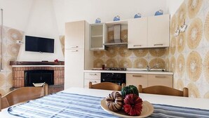 Una cocina moderna con estufa integrada, televisor de pantalla plana y comedor con mantel a rayas y calabazas decorativas.
