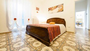 Un dormitorio con una cama grande, baldosas de suelo estampadas, una ventana con cortinas y un cuadro en la pared.