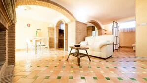 A spacious living area with a white sofa, a small round table, and a tiled floor. There are brick arches and a kitchen area visible in the background. - Casa Vacanza Polifemo Loft (Sperlonga)