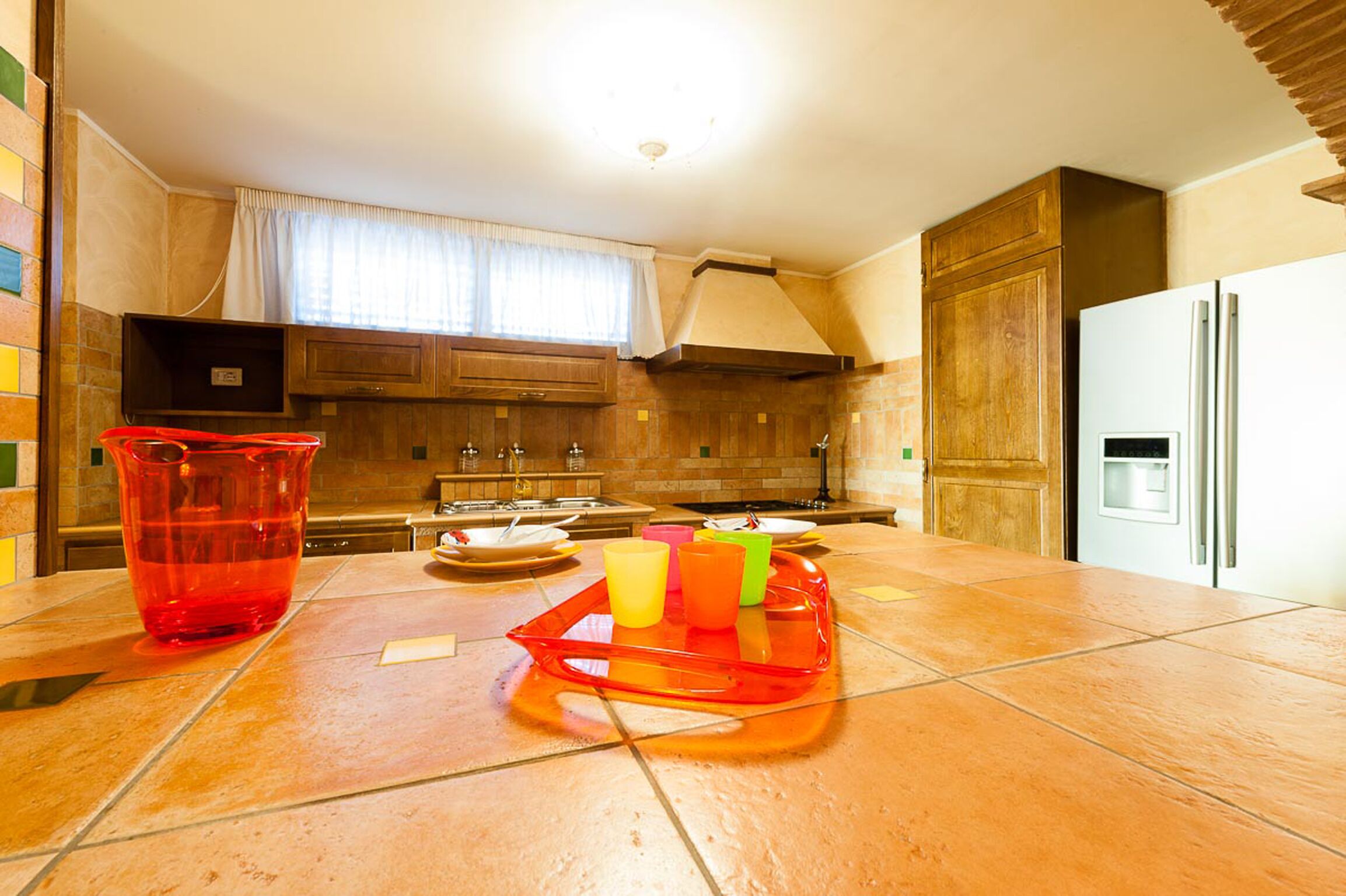 A kitchen with wooden cabinets, a tiled countertop, a sink, and a refrigerator.