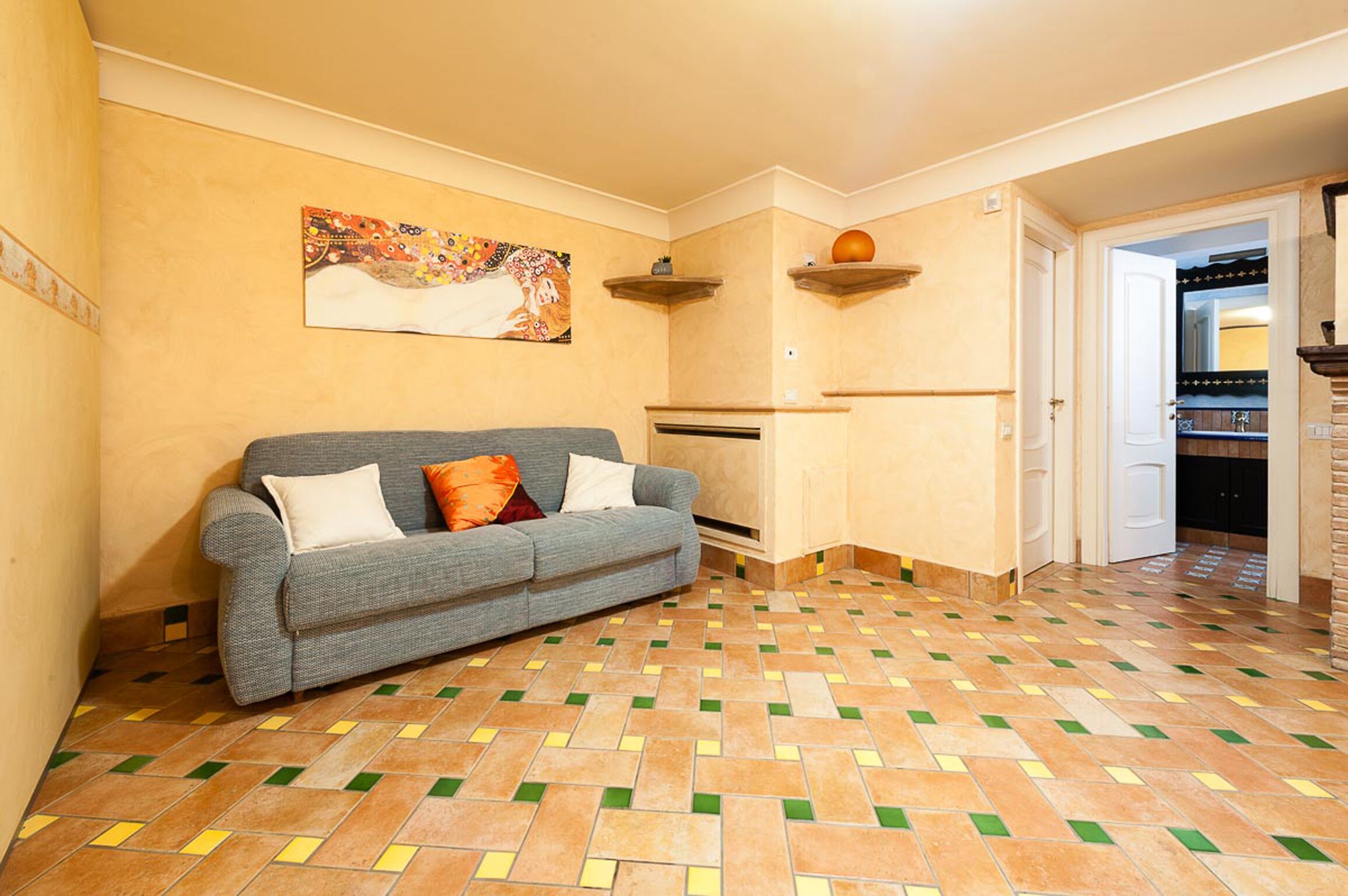 A living room with a grey sofa, patterned floor tiles, and a painting on the wall.