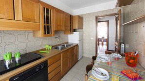 A kitchen with wooden cabinets, a black dishwasher, and a striped tablecloth. - Casa Vacanza Santa Laura (Sperlonga)