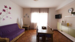 A cozy living room with a sofa, a dining table, and a TV mounted on the wall. - Casa Vacanza Santa Laura (Sperlonga)