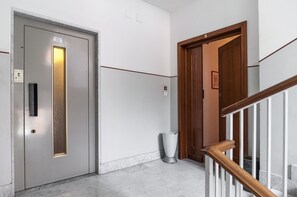 An interior hallway with a metallic elevator door, a wooden door, and a marble floor.