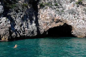 A rocky coastline with a cave entrance and clear turquoise water.