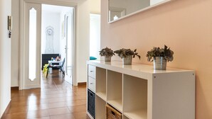A hallway with a white console table, potted plants, a clock, and a door leading to a room with a bed and a dresser. - Casa Vacanza Valle (Sperlonga)