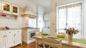 A kitchen with white cabinets, a stove, and a dining table with chairs. - Casa Vacanza Valle (Sperlonga)