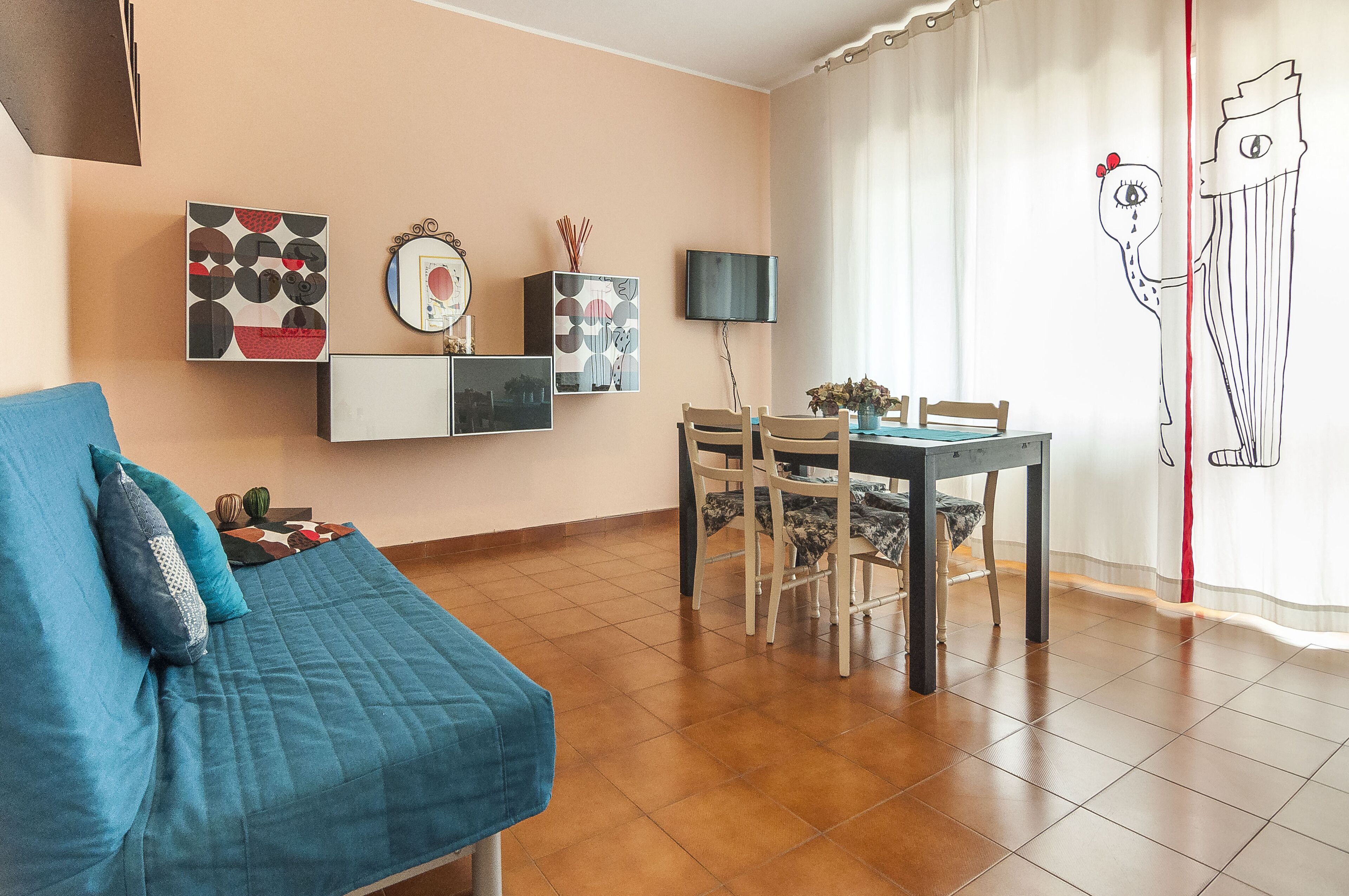 Een woonkamer met een blauwe bank, een eettafel met stoelen en wanddecoratie.