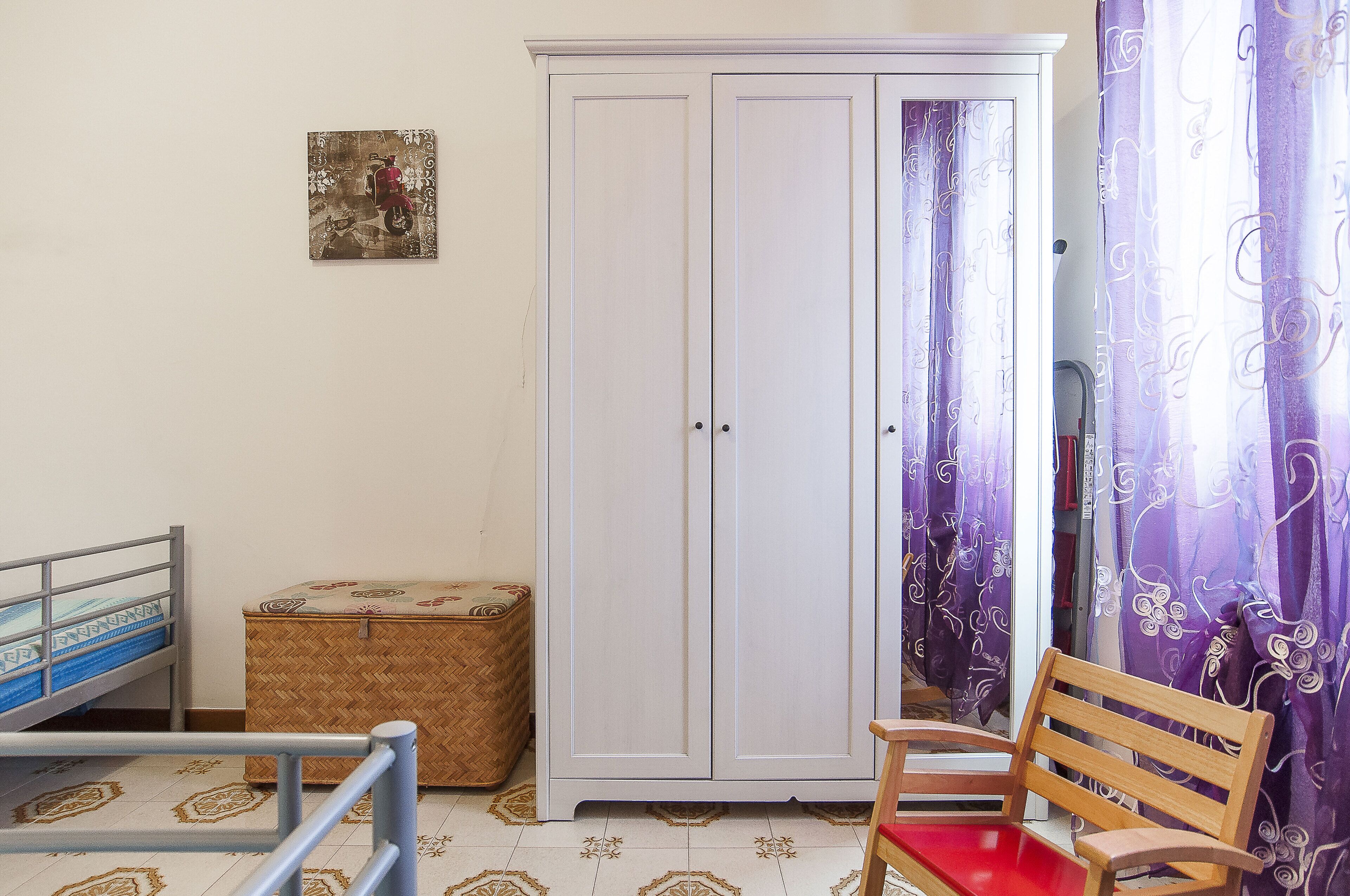 Um quarto com uma cama, um guarda-roupa, um banco e uma pequena mesa.