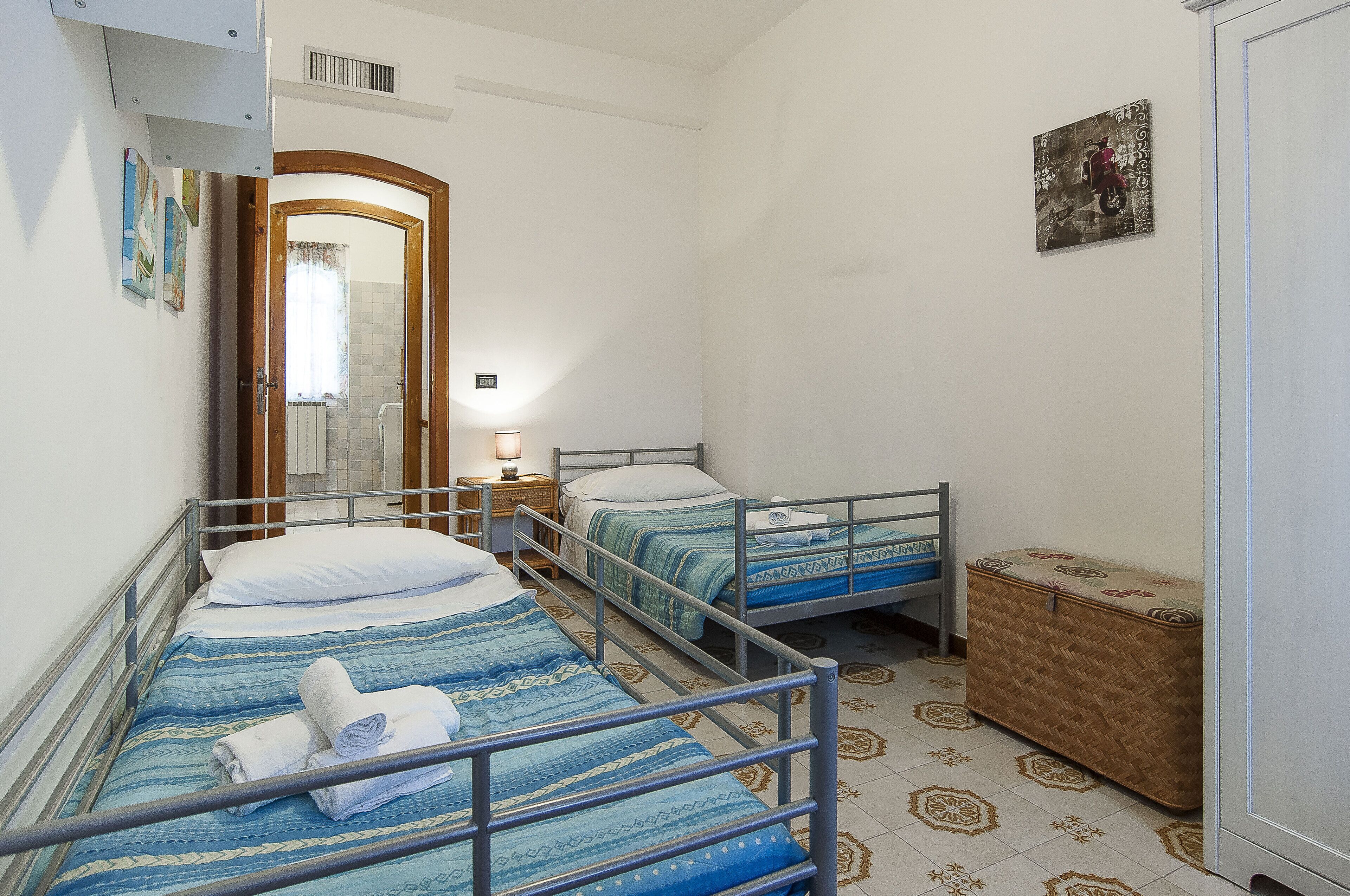 A room with three beds, a wooden wardrobe, and a small bedside table with a lamp.