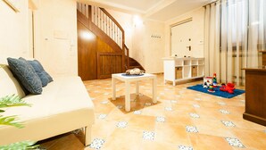 A living room with a sofa, a small table, a staircase, and a play area with toys. - Casa Vacanza Villa Polifemo (Sperlonga)