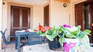 A patio with a table and chairs, potted plants, and a wooden ceiling.