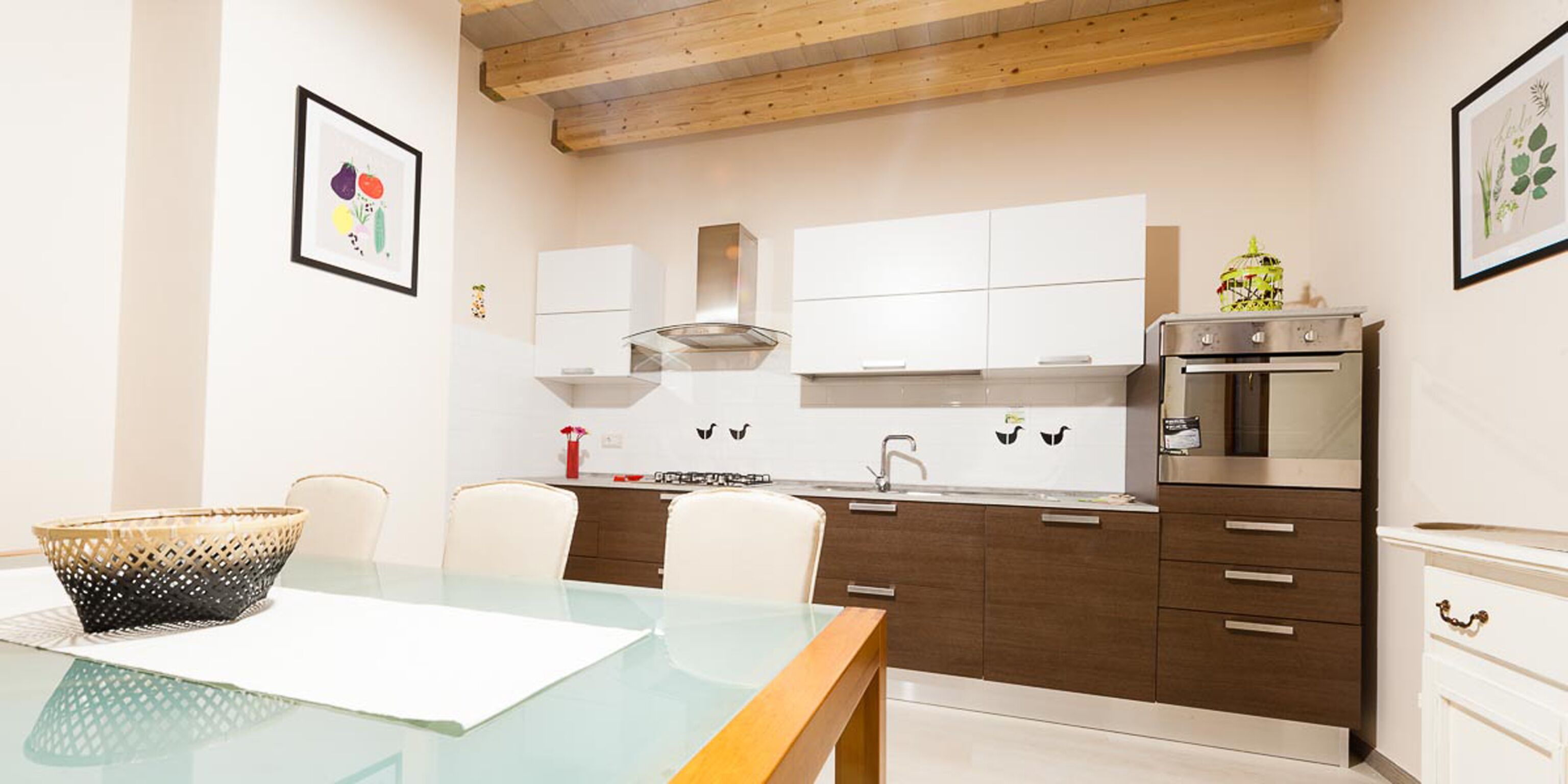 Una cocina moderna con armarios blancos, un horno de acero inoxidable y un comedor con mesa y sillas de vidrio.