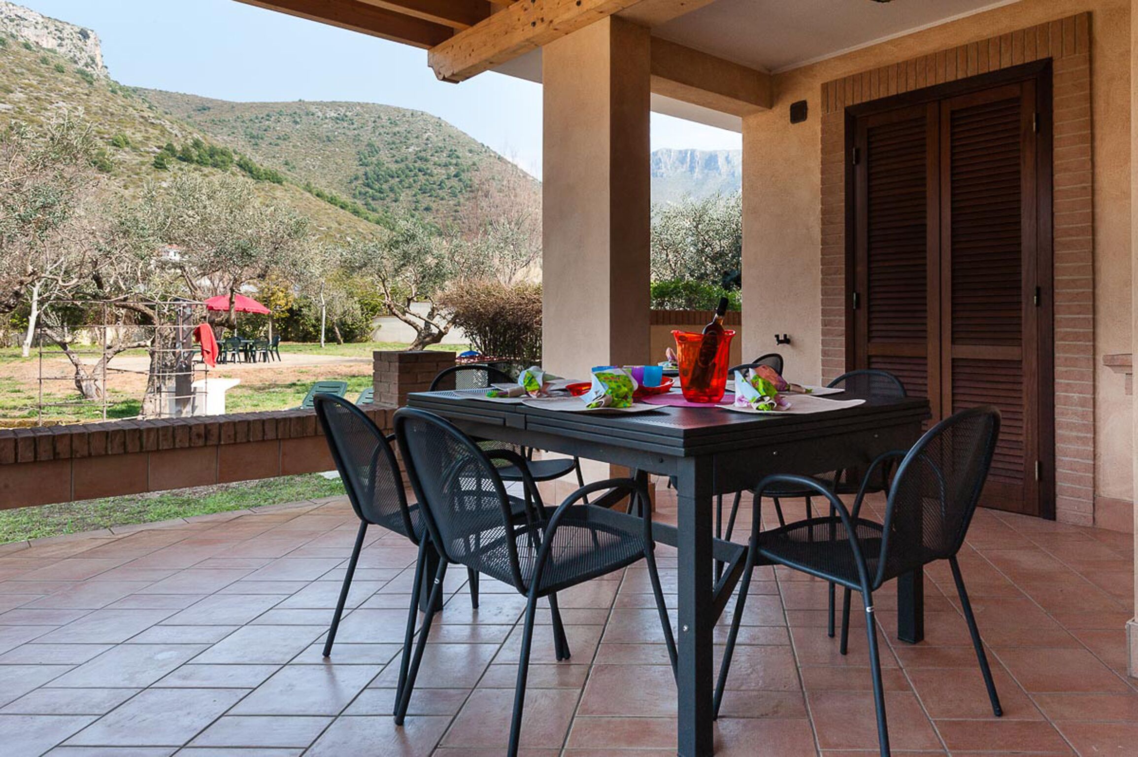 Um alpendre coberto com uma mesa e cadeiras, uma parede de tijolos e vista para uma paisagem montanhosa.