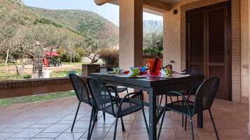 Um alpendre coberto com uma mesa e cadeiras, uma parede de tijolos e vista para uma paisagem montanhosa.