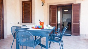 A dining area with a table set for four, surrounded by blue chairs, and a window with closed shutters. - Casa Vacanza Villa Polifemo (Sperlonga)