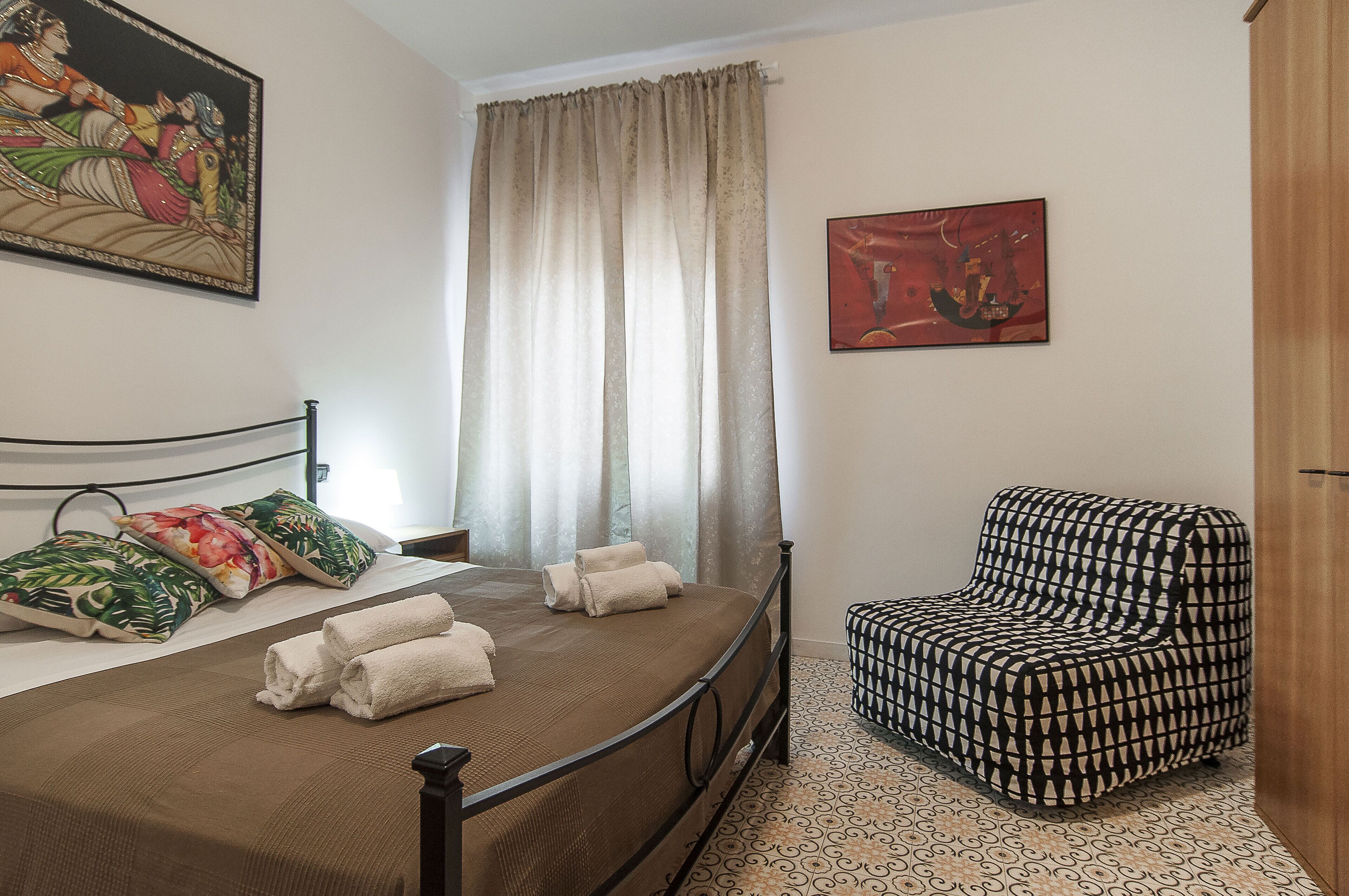 A bedroom with a bed, a chair, a painting, and a curtain.