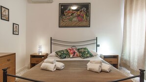 A neatly made bed with towels, a nightstand with a lamp, and a painting on the wall. - Casa Vacanza Colombo (Sperlonga)