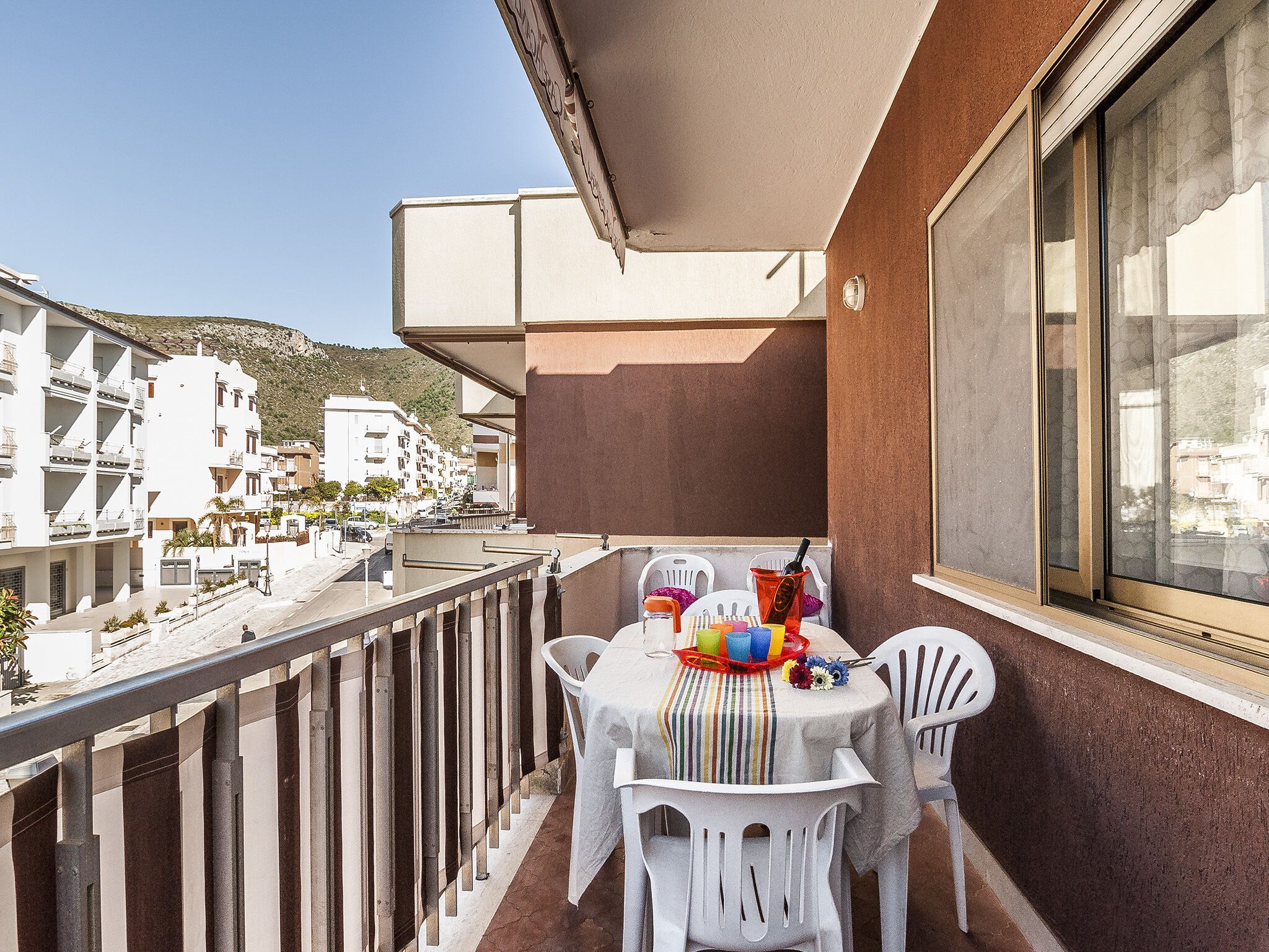A balcony with a table set for two, chairs, and a small table with a colorful cloth.