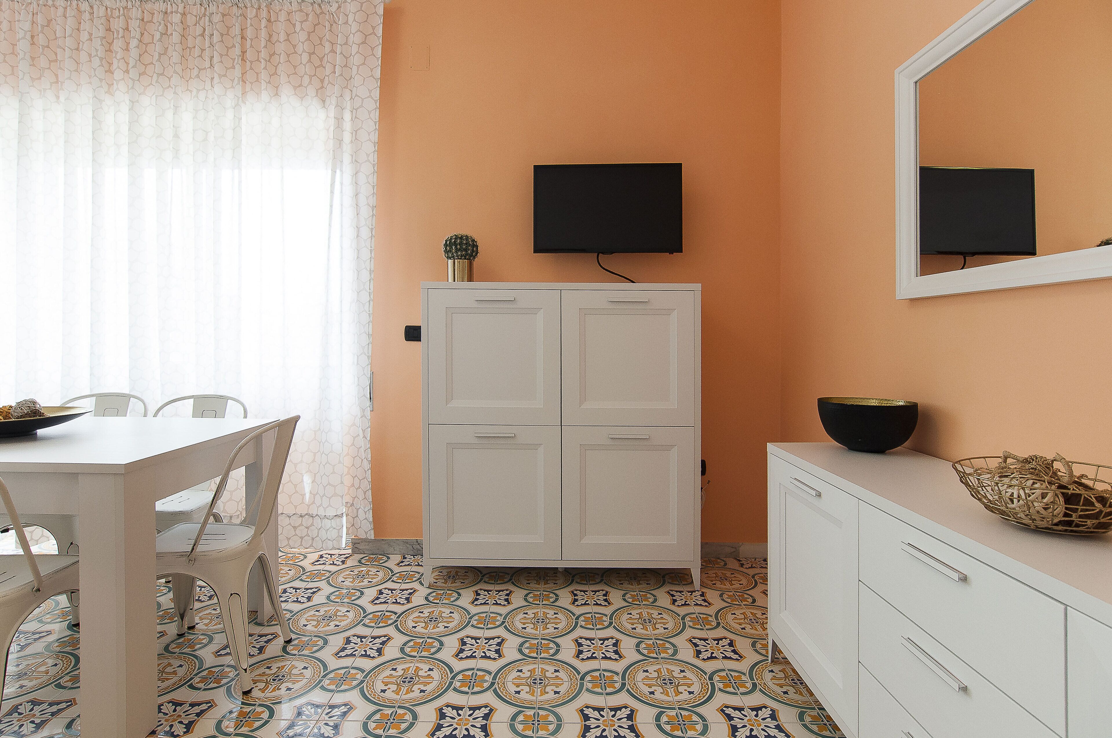 Una habitación con un armario blanco, un televisor montado en la pared y un piso con estampado.