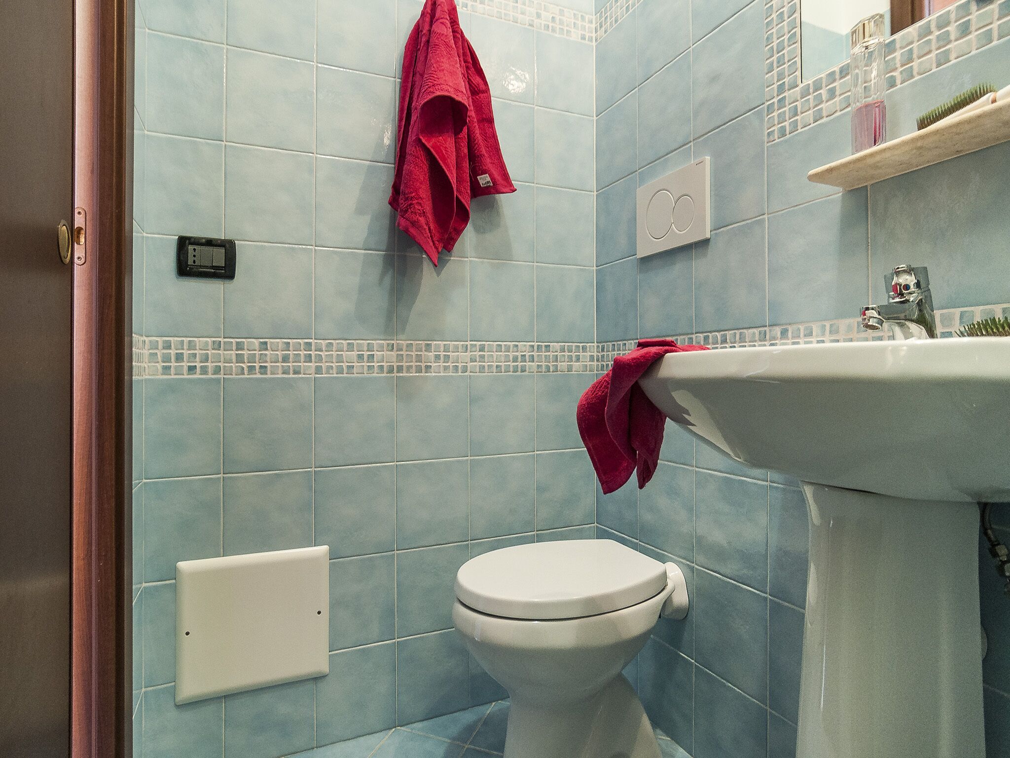 Un baño con inodoro, lavabo y toallero con una toalla roja.