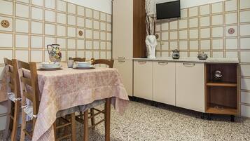 Un comedor con una mesa dispuesta para cuatro personas, un reloj en la pared y un televisor sobre un mueble.