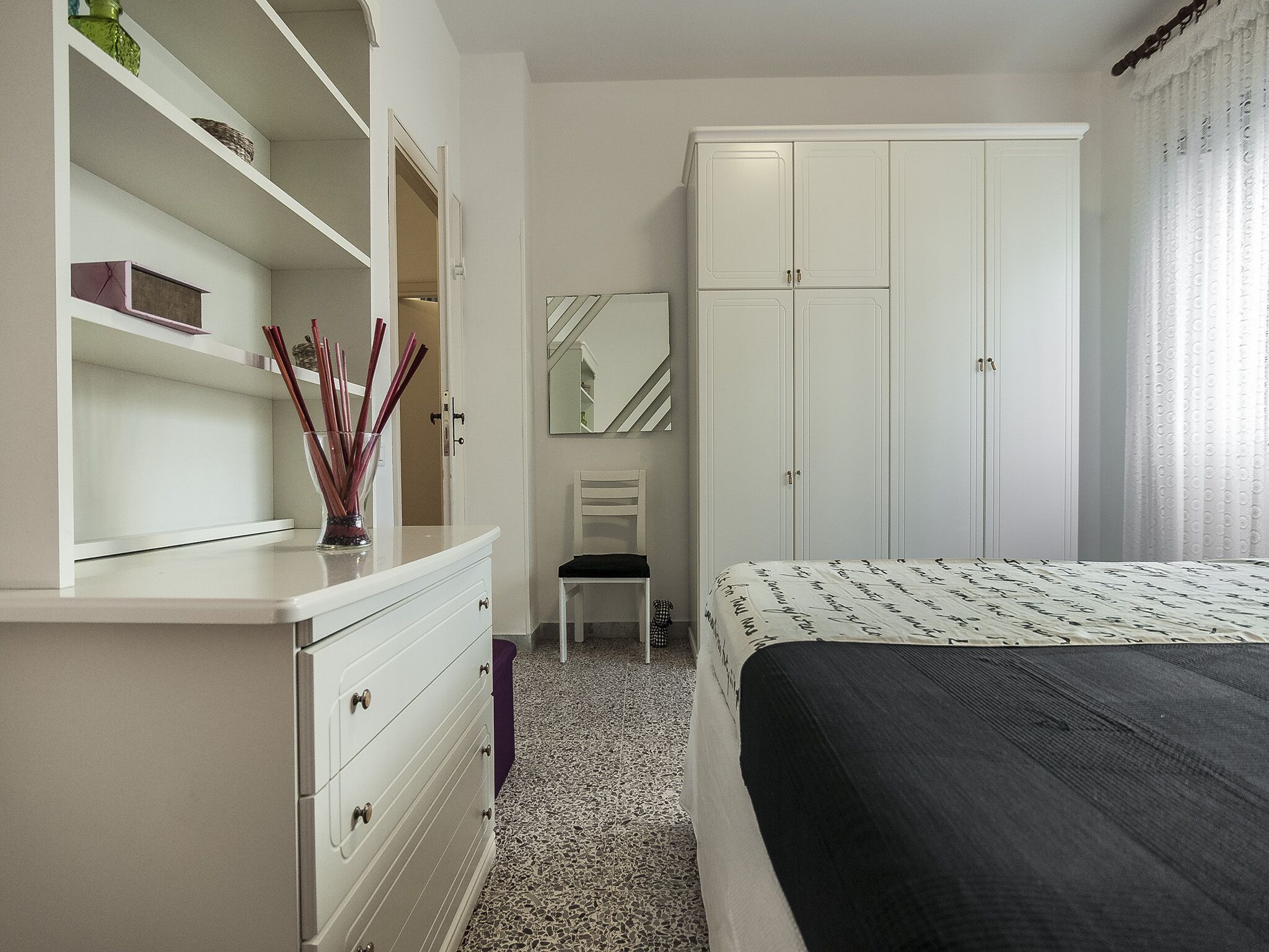Um quarto com uma cama, cômoda, cadeira e guarda-roupa.