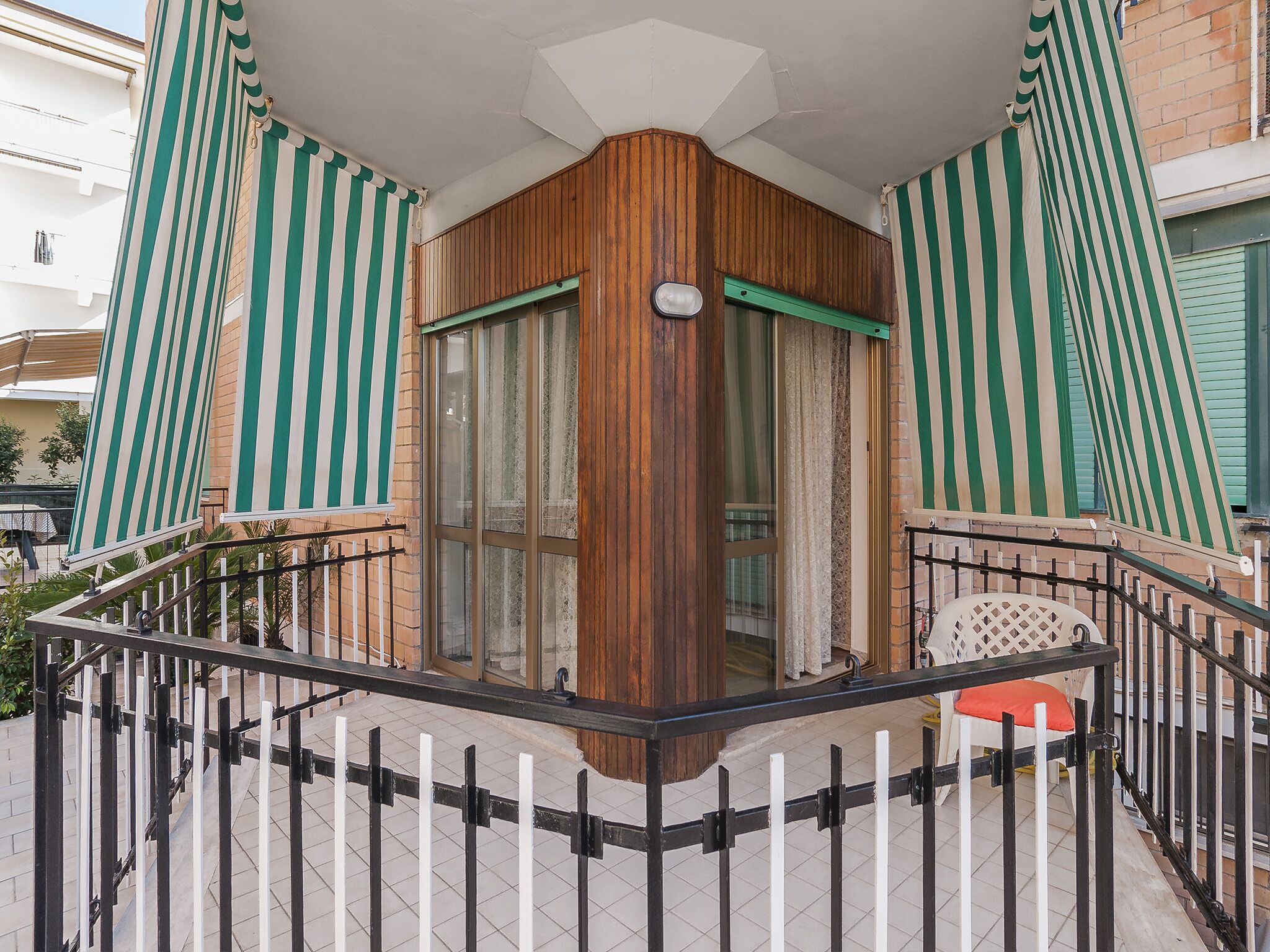 Varanda nos cantos com painéis de madeira, porta de vidro e cortinas listradas.