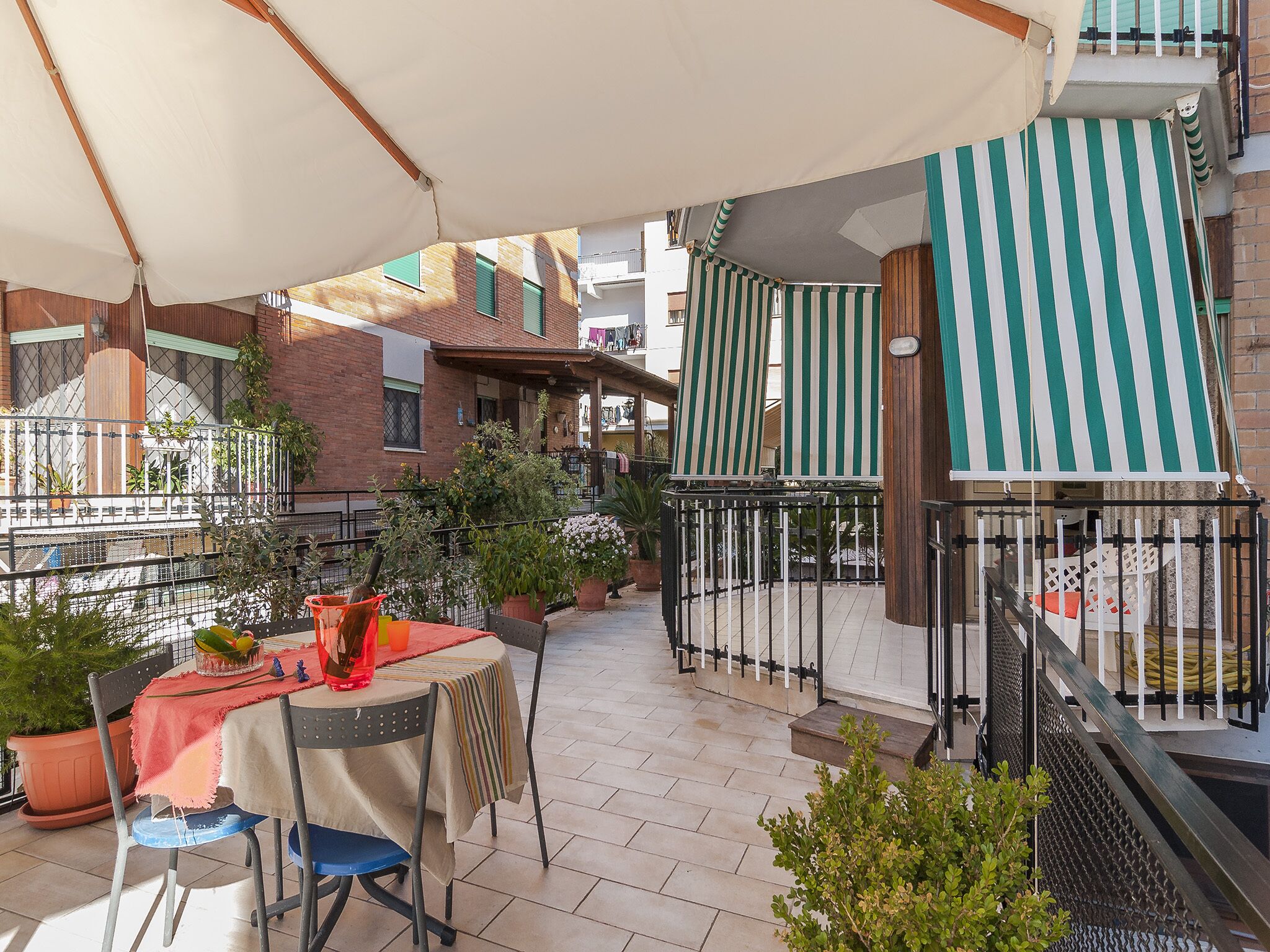 Un espace patio aménagé avec une table et des chaises, des plantes en pot et des auvents à rayures qui offrent de l’ombre.