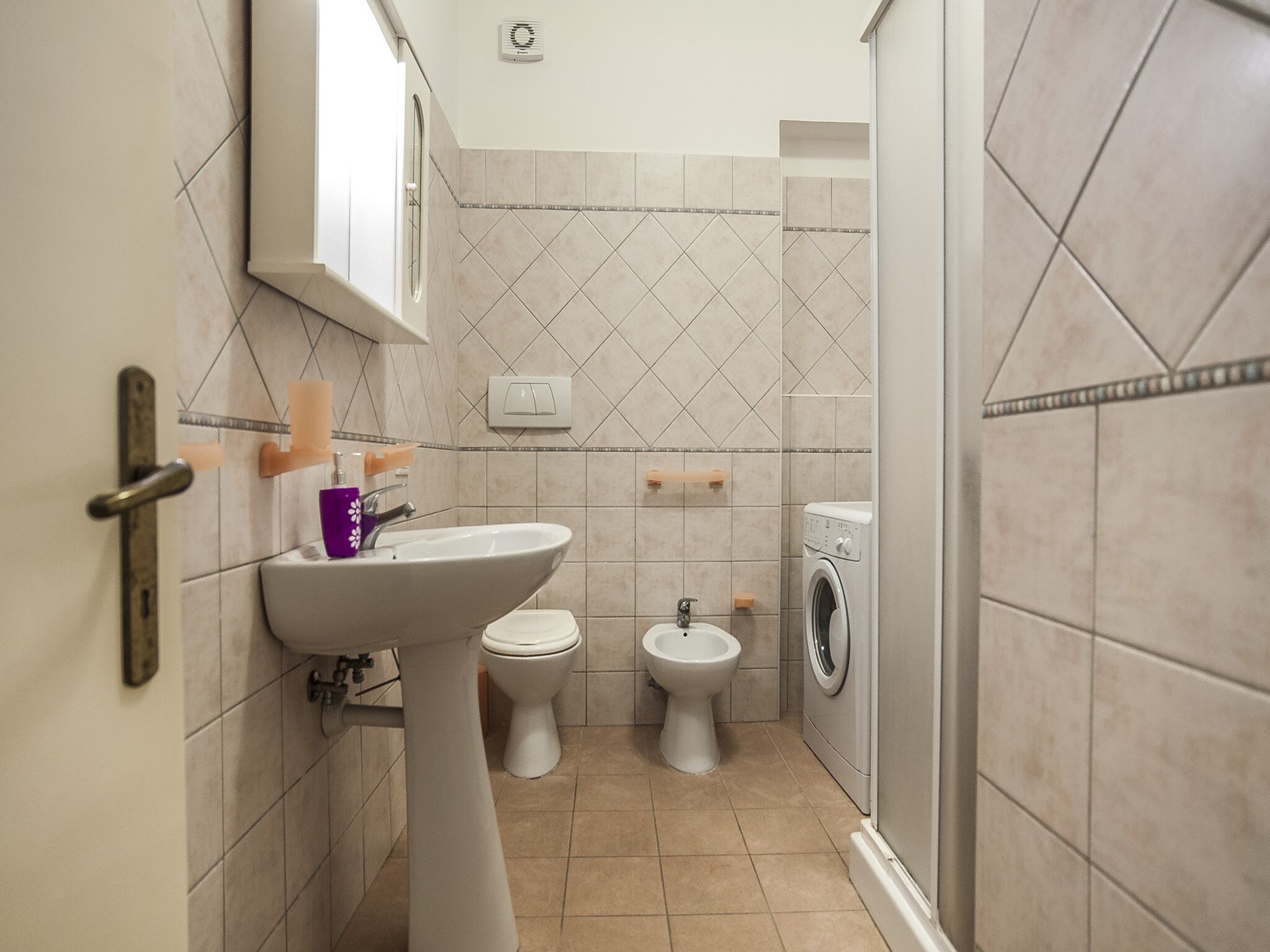 Un baño pequeño con lavamanos, dos inodoros y lavadora.