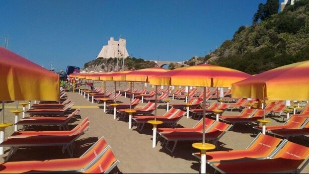 A beach with rows of sun loungers and umbrellas, a castle-like structure in the background, and a clear sky. - Casa Vacanza Vespucci 3 (Sperlonga)