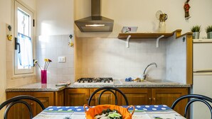 A kitchen with a gas stove, sink, and wooden cabinets. There is a table with a blue and white tablecloth and a basket of vegetables. - Casa Vacanza Vespucci 3 (Sperlonga)