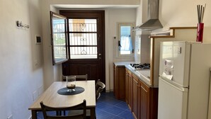 A compact kitchen with a dining table, chairs, a refrigerator, and a window with a view of the outside. - Casa Vacanza Vespucci 3 (Sperlonga)