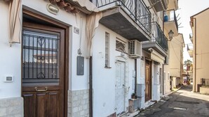 A narrow street with buildings featuring traditional architecture, including a wooden door and a balcony with a metal railing. - Casa Vacanza Vespucci 3 (Sperlonga)