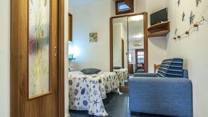 A compact room with a bed, a sofa, a TV on a shelf, and a door with a decorative glass panel. - Casa Vacanza Vespucci 3 (Sperlonga)