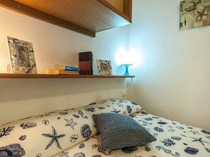 A bedroom with a bed featuring a nautical-themed bedspread, a bedside table with books and a lamp, and a wall with a framed picture. - Casa Vacanza Vespucci 3 (Sperlonga)