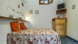 A bedroom with a bed, orange pillows, a wooden dresser, a TV on a shelf, and wall art. - Casa Vacanza Vespucci 4 (Sperlonga)