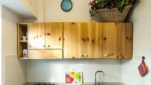 A kitchen with wooden cabinets, a gas stove, a sink, and a clock on the wall. - Casa Vacanza Vespucci 4 (Sperlonga)