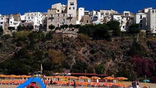 A coastal town with buildings on a hillside, beach umbrellas, and a lifeguard tower. - Casa Vacanza Vespucci 4 (Sperlonga)
