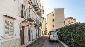A narrow street lined with multi-story buildings, a parked van, and a hedge along the right side. - Casa Vacanza Vespucci 4 (Sperlonga)
