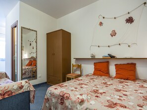 A bedroom with a bed, a wardrobe, a chair, a mirror, and a shelf with books and decorative items. - Casa Vacanza Vespucci 4 (Sperlonga)